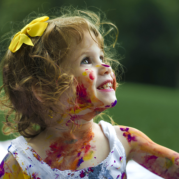 bambina con la faccia macchiata di tempera colorata ride mentre guarda in alto